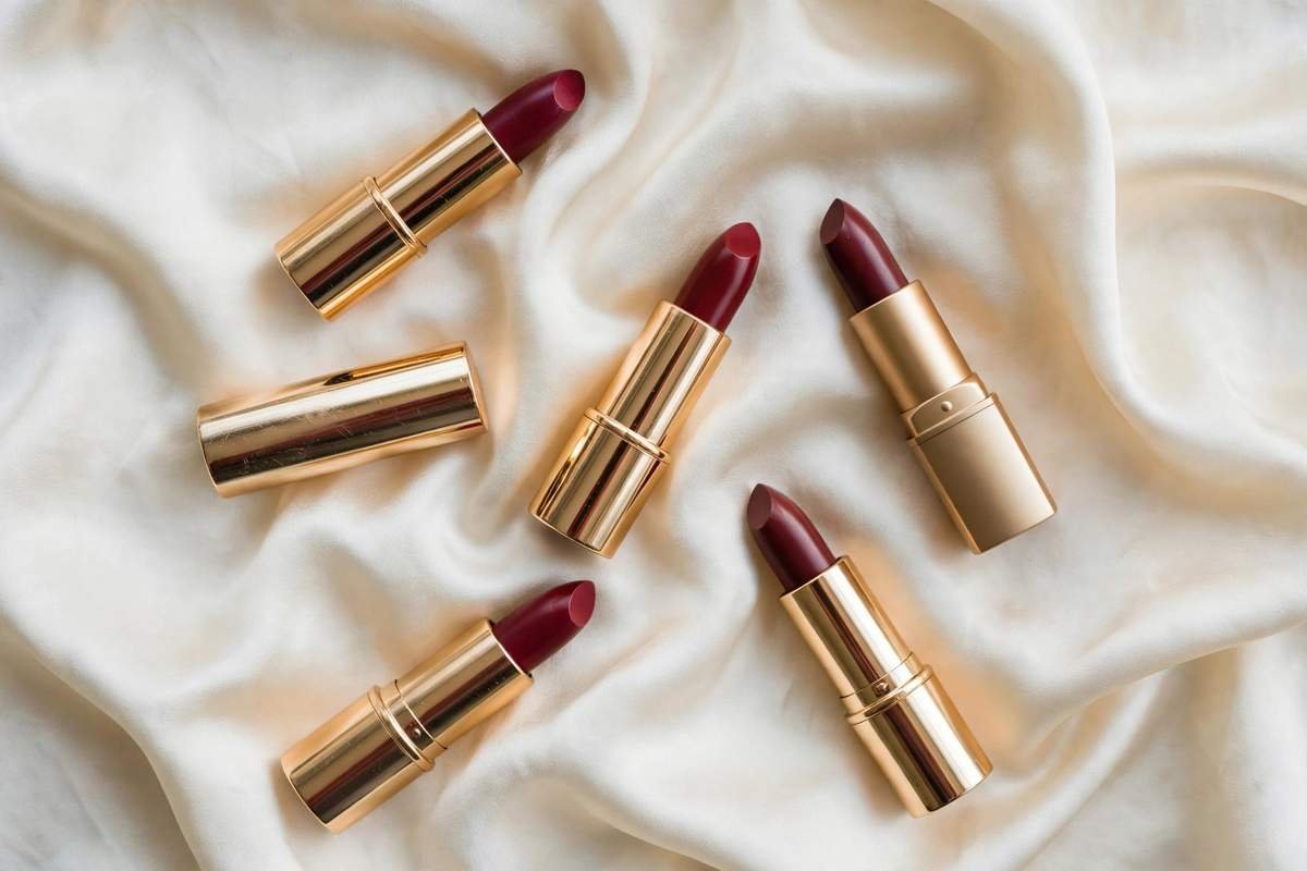 Flat lay of berry-toned lipsticks in cranberry shades on cream silk