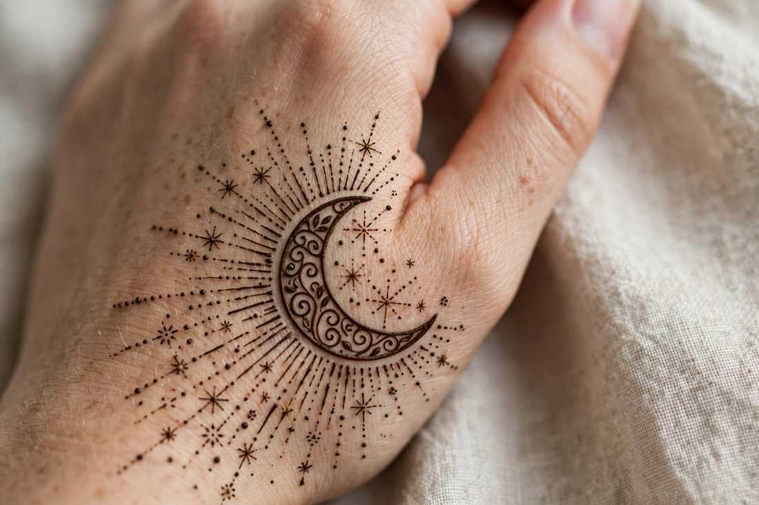 Henna crescent moon design on the side of a hand with stars